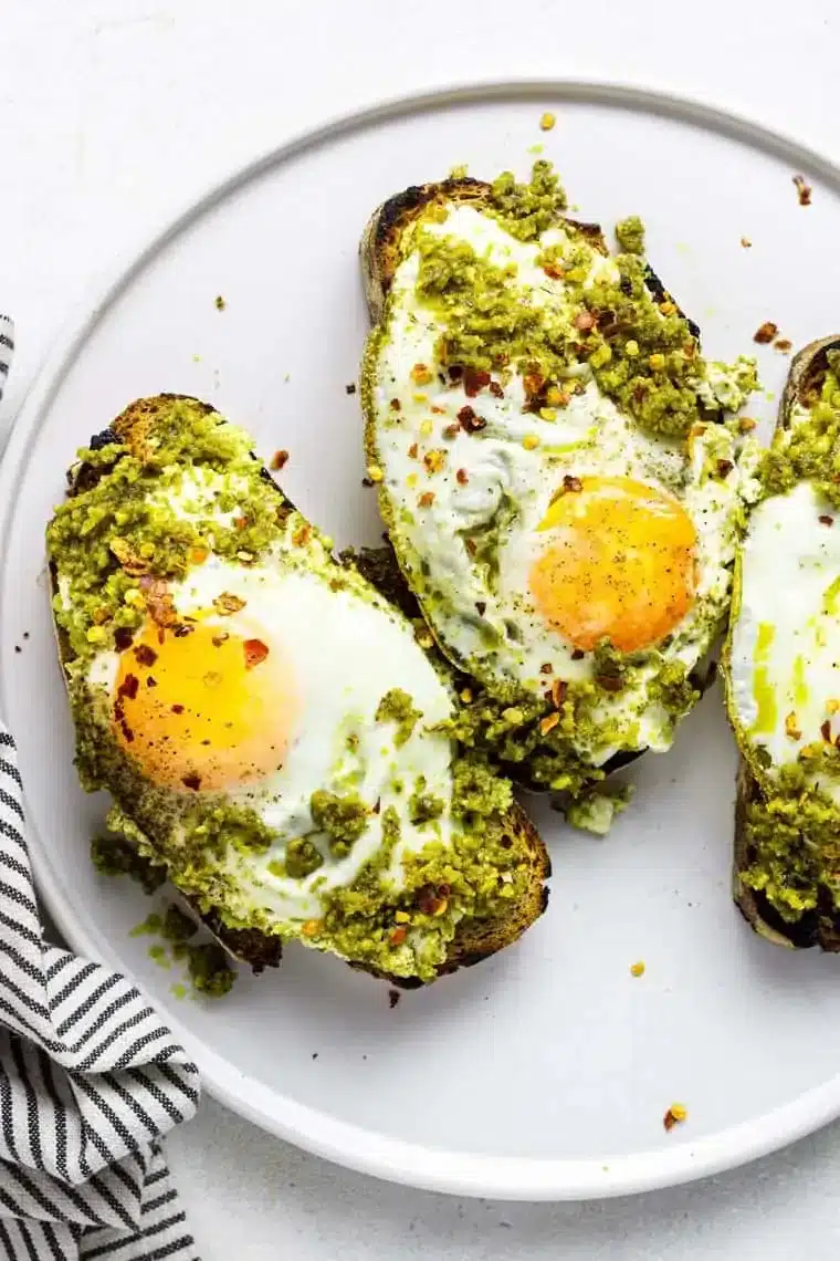 Delicious pesto eggs served on a plate with fresh herbs and toast.