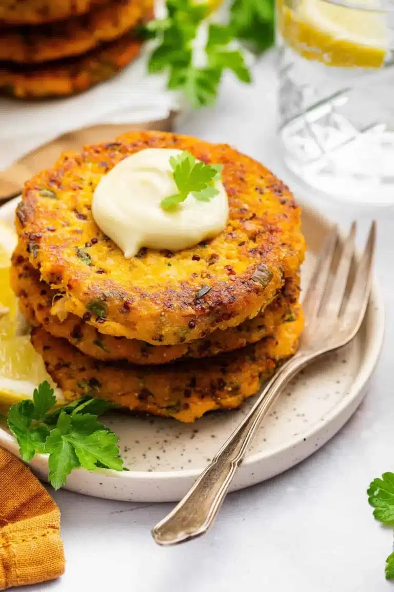 Plate of crispy salmon patties served with dipping sauce and garnished with herbs